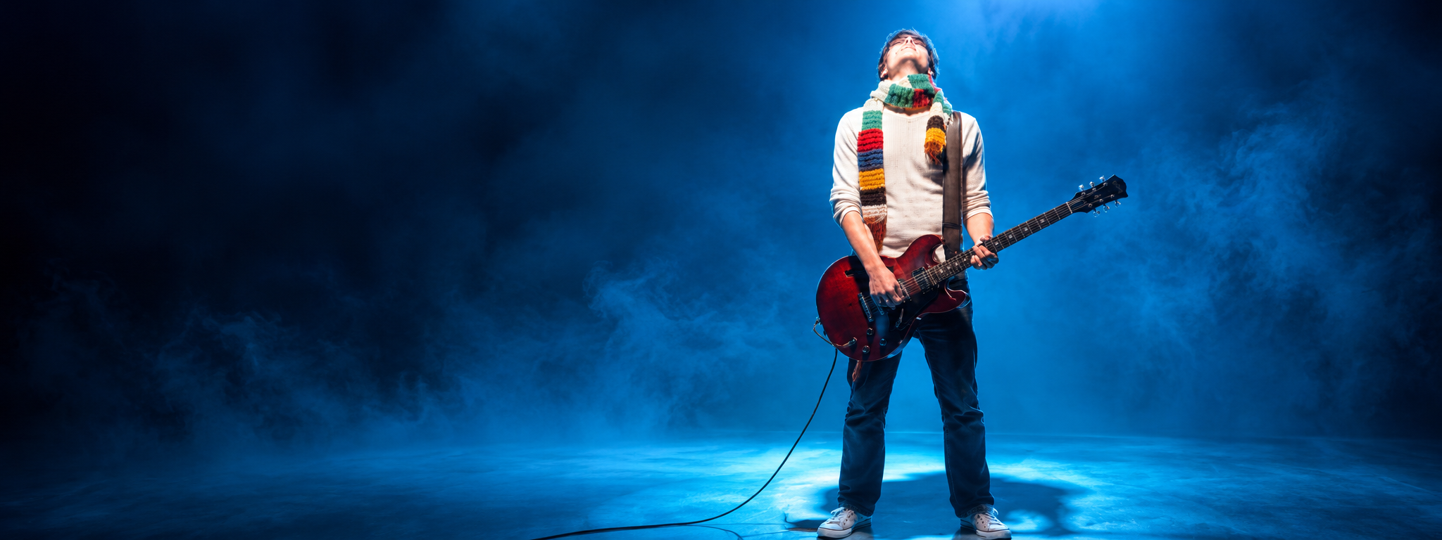 Guitarist leaning back into a performance on a blue-lit stage